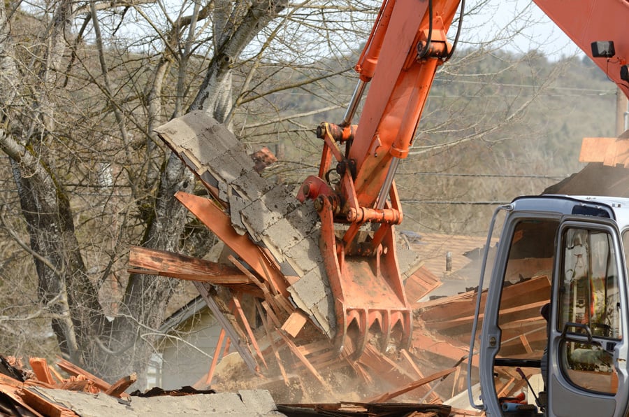 Exterior structural demolition in Calgary with an excavator tearing down a building’s roof and exterior walls.